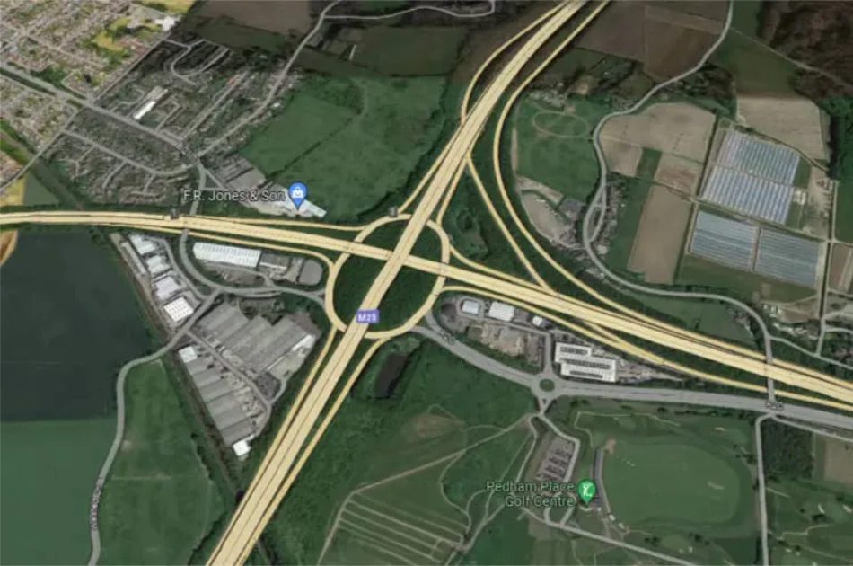 Aerial view of the M25 motorway interchange, showing connecting roads, nearby industrial buildings, and a golf course.
