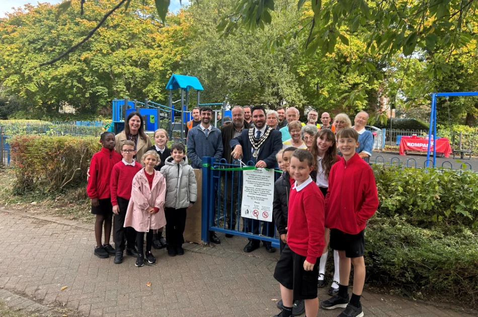 A group of children and adults standing at the Hilda May Playground entrance for a ribbon-cutting ceremony.